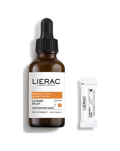 Frasco con cuentagotas de la base del Sérum Concentrado Protocolo Luminosidad de Lierac junto a un sobre de vitamina C, sobre fondo blanco