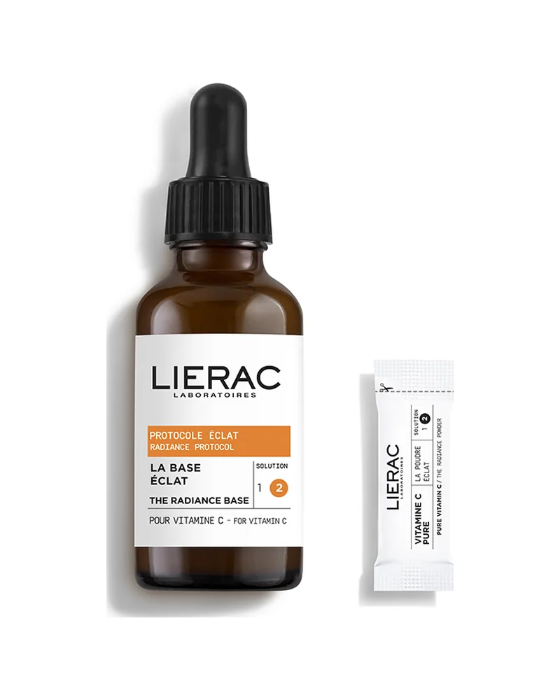 Frasco con cuentagotas de la base del Sérum Concentrado Protocolo Luminosidad de Lierac junto a un sobre de vitamina C, sobre fondo blanco