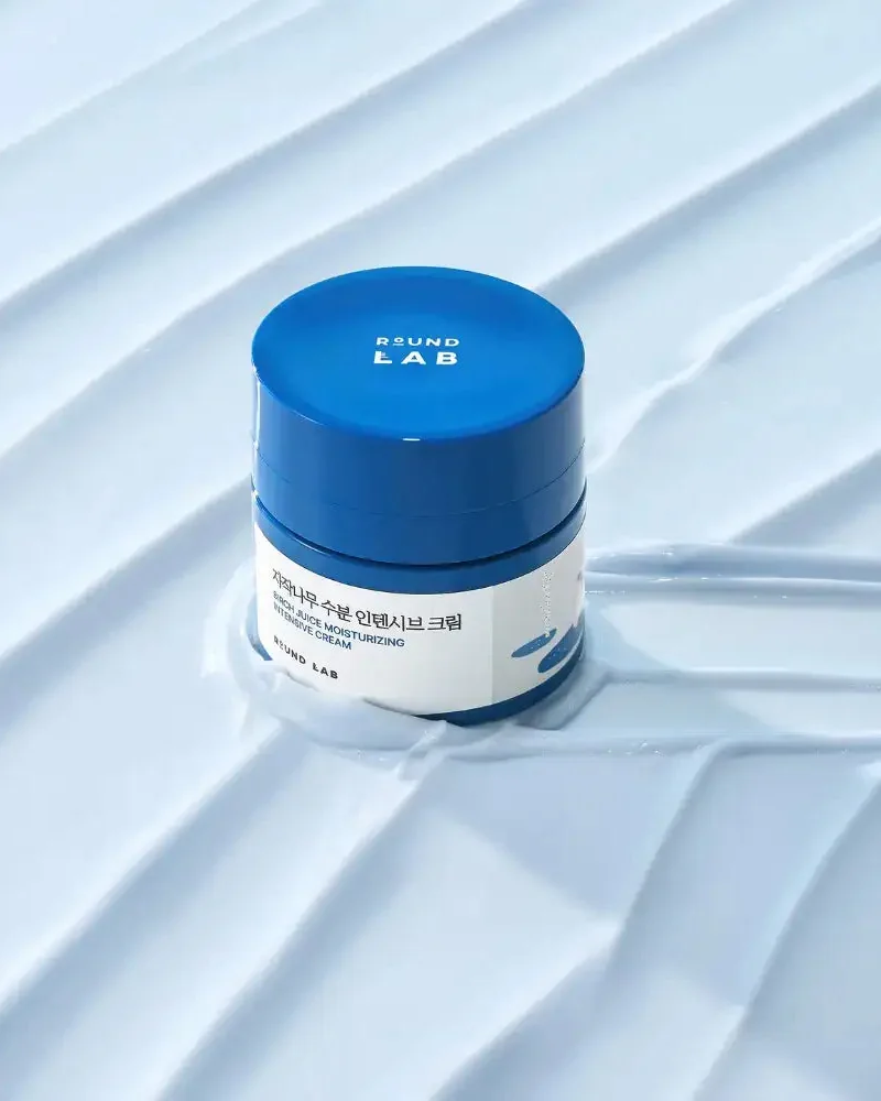 Tarro de Birch Moisturizing Intensive Cream sobre una textura de crema azul claro